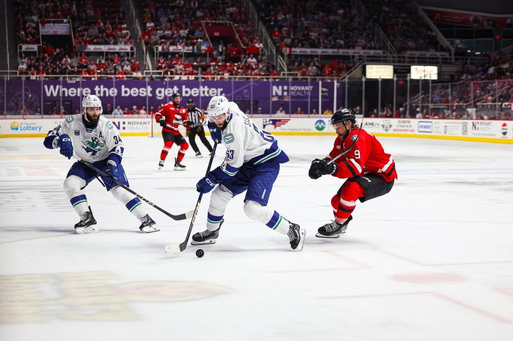 Abbotsford Canucks forward Max Sasson (63) skates up ice with the puck while Charlotte Checkers forward Rasmus Asplund (9) follows. (Photo Credit: @TheAHL/X) 