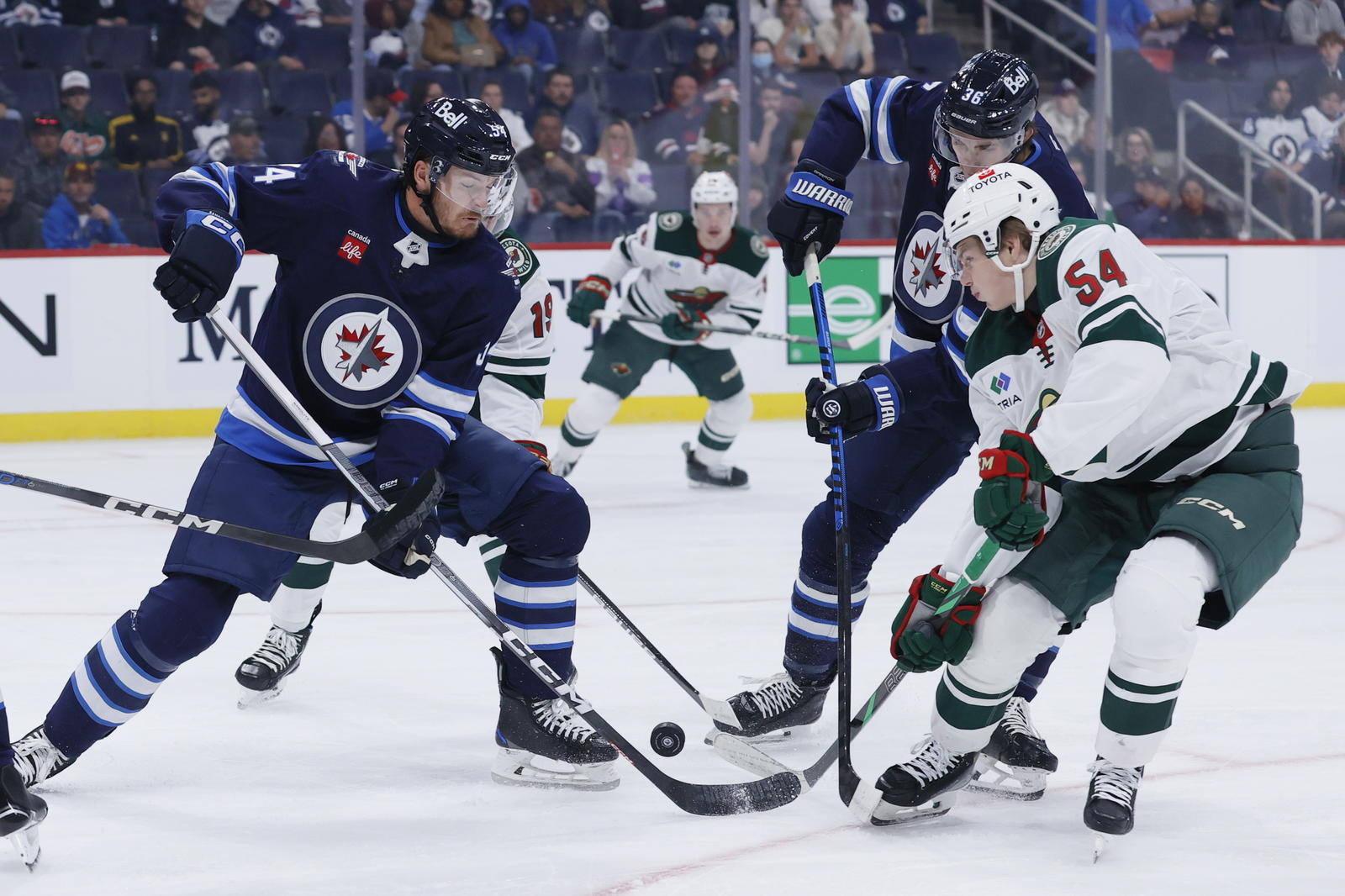 Sep 21, 2024; Winnipeg, Manitoba, CAN; Winnipeg Jets defenseman Dylan Samberg (54) and Minnesota Wild forward Ryder Ritchie dig for the puck in the first period at Canada Life Centre. Mandatory Credit: James Carey Lauder-Imagn Images