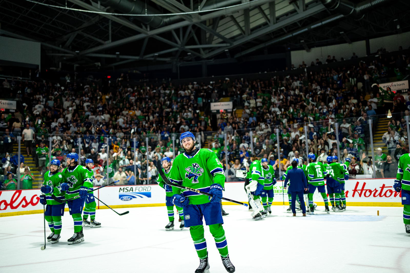 Abbotsford Canucks Linus Karlsson (94) smiles while on the ice. In the background, fans wave towels to celebrate the team's win. (Photo Credit: @AbbyCanucks/X) 