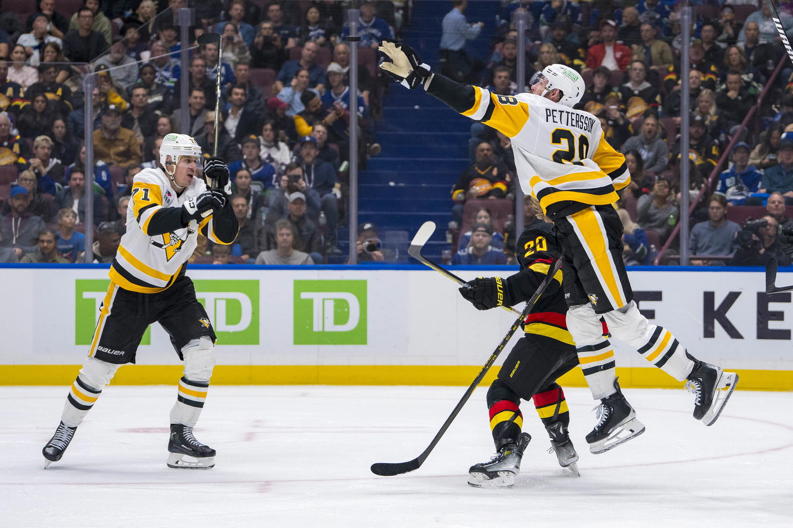 Oct 26, 2024; Vancouver, British Columbia, CAN; Vancouver Canucks forward Danton Heinen (20) and Pittsburgh Penguins forward Evgeni Malkin (71) watch as defenseman Marcus Pettersson (28) leaps to catch the flying puck during the third period at Rogers Arena. Mandatory Credit: Bob Frid-Imagn Images