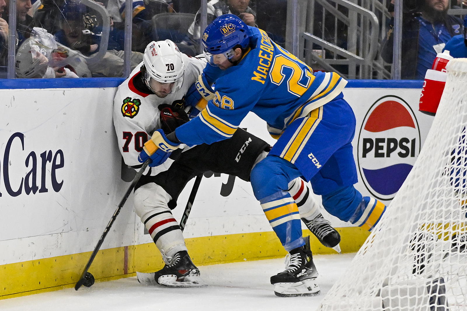 Dec 23, 2023; St. Louis, Missouri, USA; St. Louis Blues left wing Mackenzie MacEachern (28) checks Chicago Blackhawks center Cole Guttman (70) during the second period at Enterprise Center. Mandatory Credit: Jeff Curry-Imagn Images